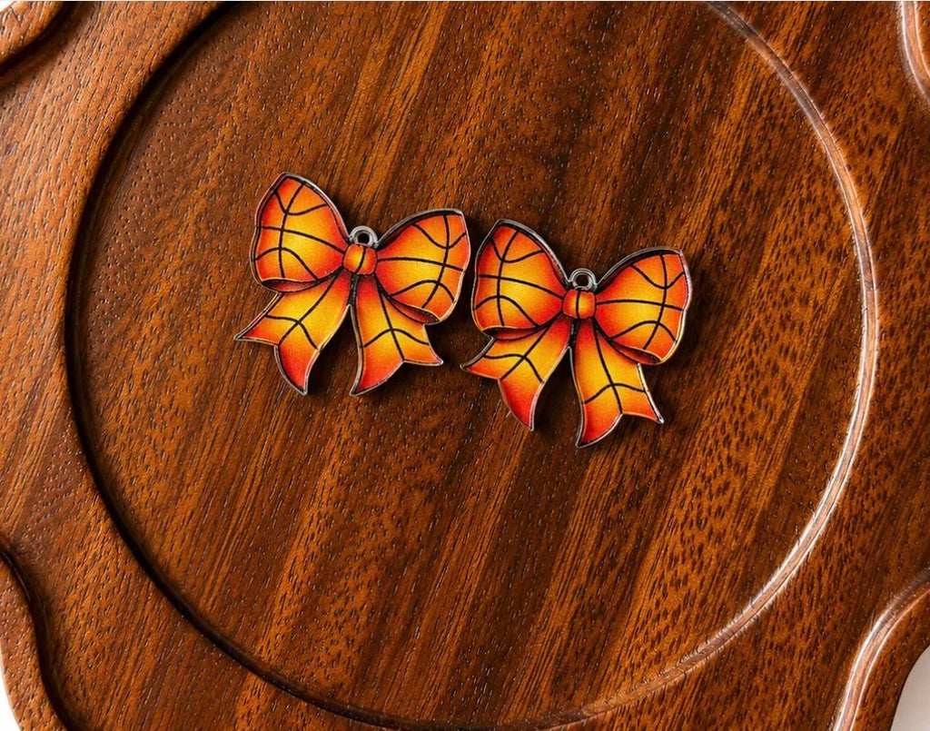 A pair of bow-shaped earrings with orange and yellow stained-glass style panels outlined in black, displayed on a round wooden surface.