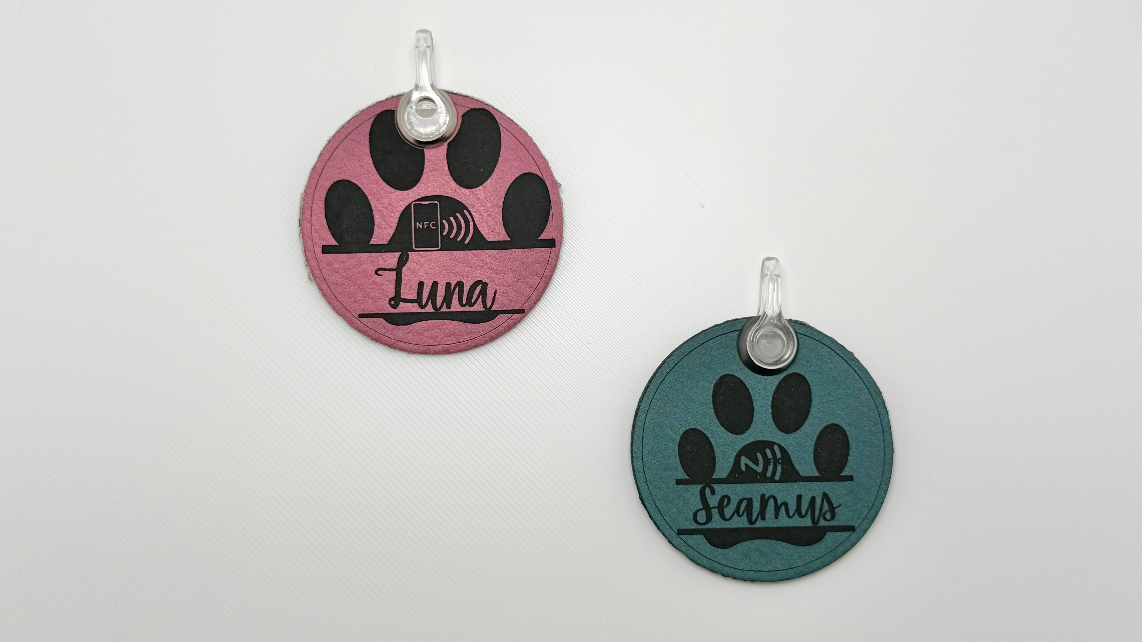 Two round retractable dog leash collars on a light gray background, one in pink with black paw prints and the name 'Luna', and one in teal with black paw prints and the name 'Beverly'.