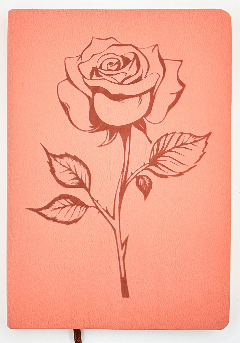 A coral pink hardcover notebook featuring a dark red line art illustration of a rose on the front cover, shown against a plain white background.