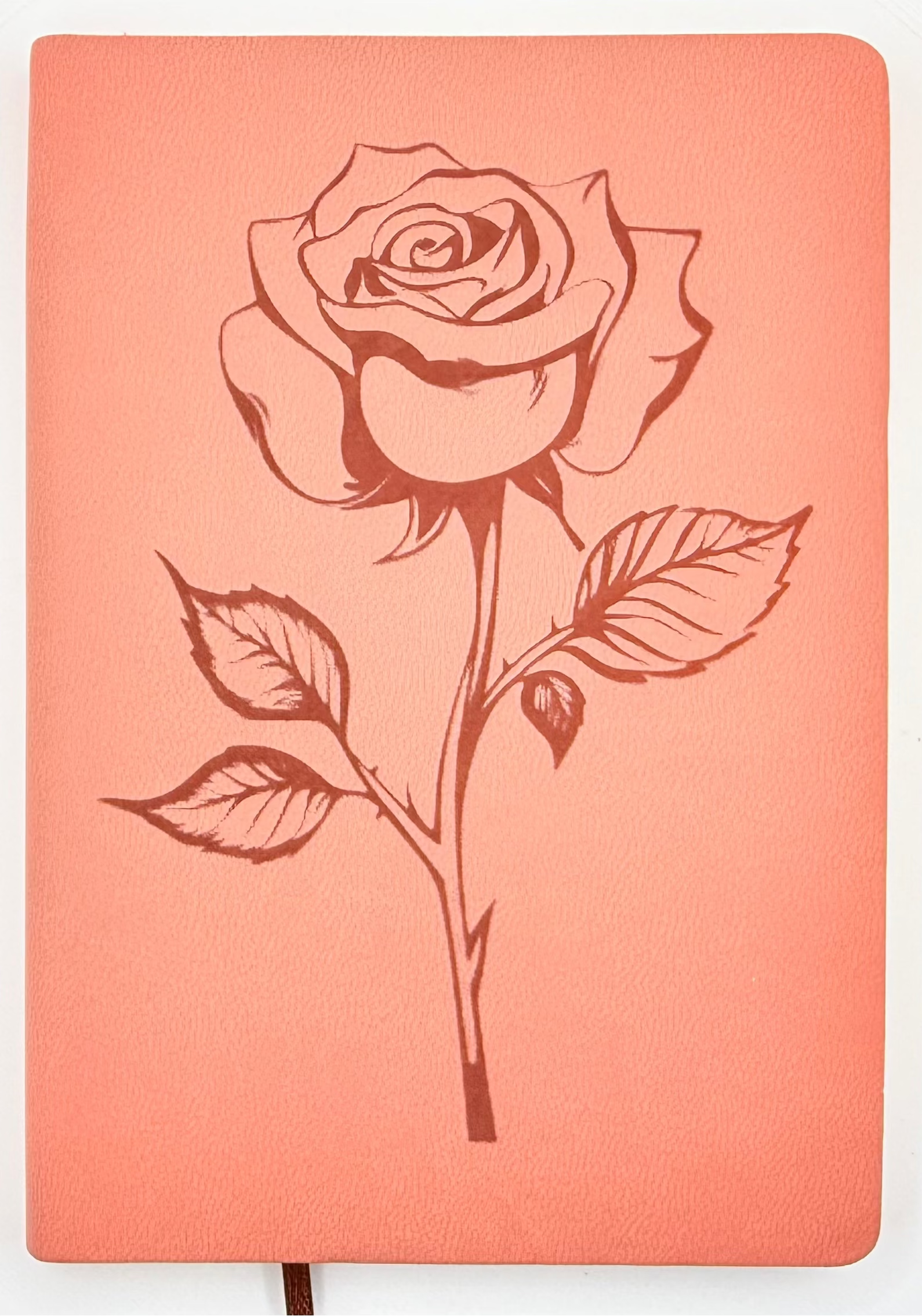 A coral pink hardcover notebook featuring a dark red line art illustration of a rose on the front cover, shown against a plain white background.