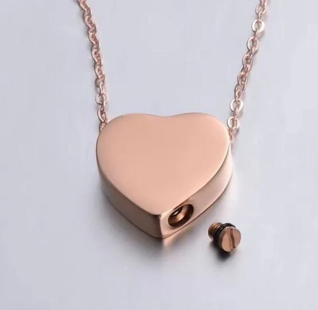 A rose gold heart-shaped pendant necklace with a matching chain and a small separate screw-back stud, shown on a light gray background.