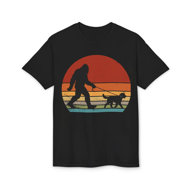 A black short-sleeve crewneck t-shirt featuring a retro-style graphic of Bigfoot walking a dog in silhouette against a multi-colored sunset gradient.