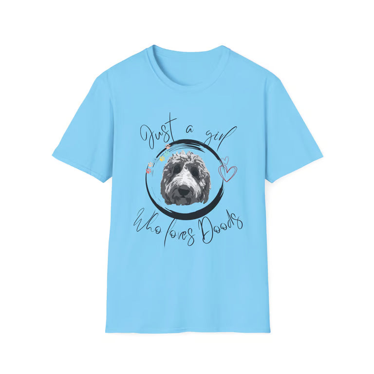 A light blue short-sleeve crewneck t-shirt featuring a graphic print of a black and white dog inside a black circle, surrounded by the text 'Just a girl who loves Dogs' in black script with small pink and blue floral accents.